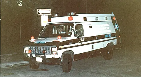 A Texas A&M Emergency Care Team ambulance, a converted van, parked at night with its warning lights lit.