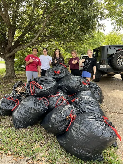 Students standing behind a large pile of full black yard-waste bags next to a truck.