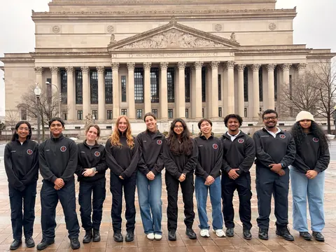 Team members in matching dark jackets lined up in front of a columned building in Washington, D.C.
