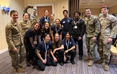Team members in dark uniform shirts posing indoors with uniformed military personnel.